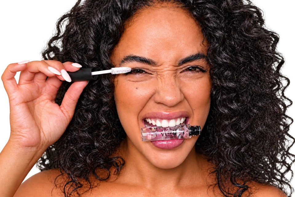 Donna che applica il mascara con scovolino e flacone YUMI